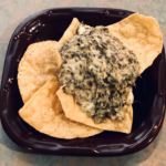 small brown plate with several tortilla chips and a small mound of spinach artichoke dip in the middle of the chips