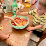 two children stirring fruit and juices in a large mixing bowl.