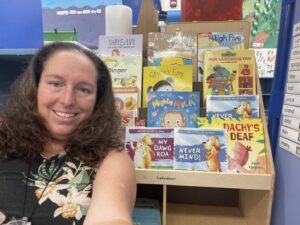 smiling teacher with childrens book covers in background